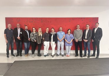 Teilnehmer der Abschlussbesprechung vor einem roten Bild