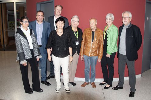 Gruppenbild mit 8 Personen vor einer roten Wand