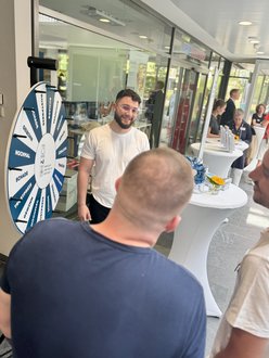 links im Bild steht ein Glücksrad - davor sieht man zwei Menschen