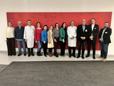 Teilnehmer der Abschlussbesprechung vor einem großen roten Bild