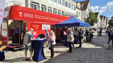 roter Infobus mit Stehtisch und Menschenansammlung davor