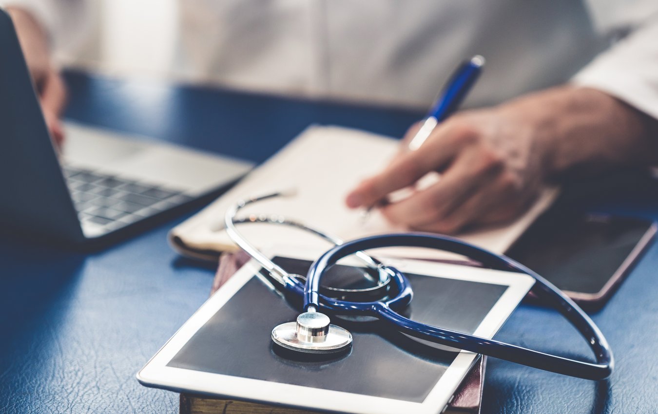 Schreibtisch eines Arztes miut Stethoskop und Laptop